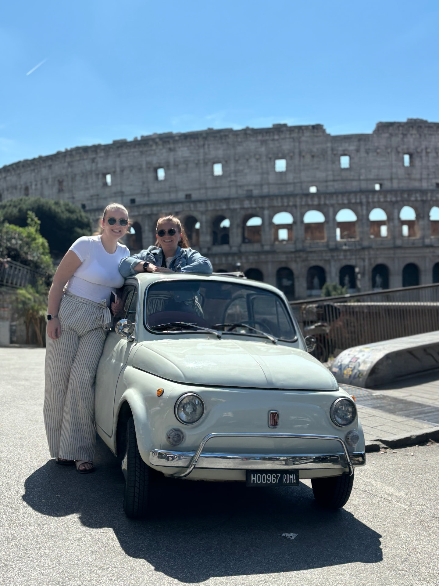 Hayley and Melissa with a vintage Fiat by the Colosseum in Rome